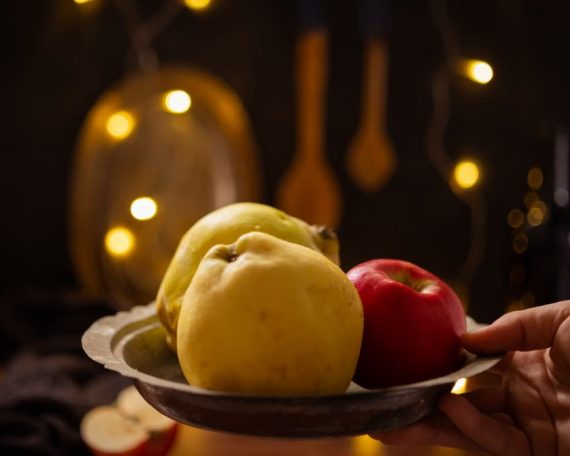 A rustic composition featuring apples and quince illuminated by warm fairy lights indoors.